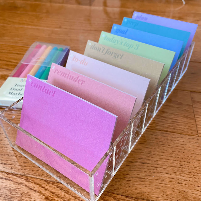 Erin Condren planning sticky notes in a clear acrylic compartment with markers on a wooden surface.