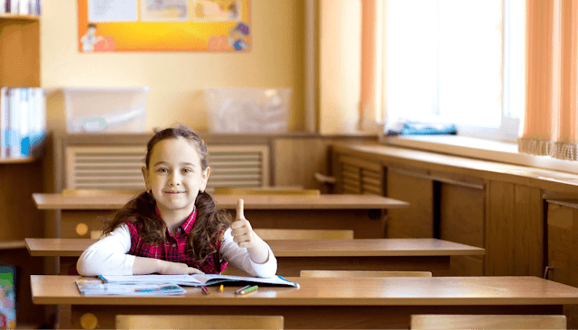 Photo of girl in classroom giving the camera thumbs-up.
