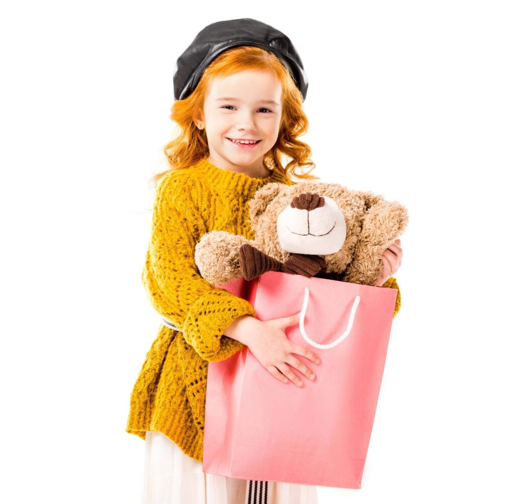 Girl carrying a paper bag with a teddy bear inside.