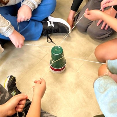 Students using string and an elastic to move stacked Solo cups