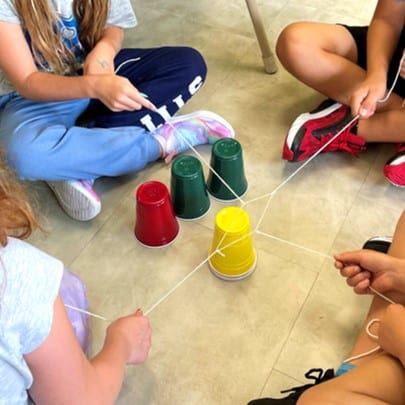 Students using string and an elastic to move stacked Solo cups