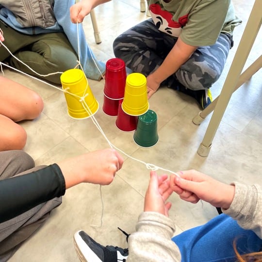 Students using string and an elastic to move stacked Solo cups